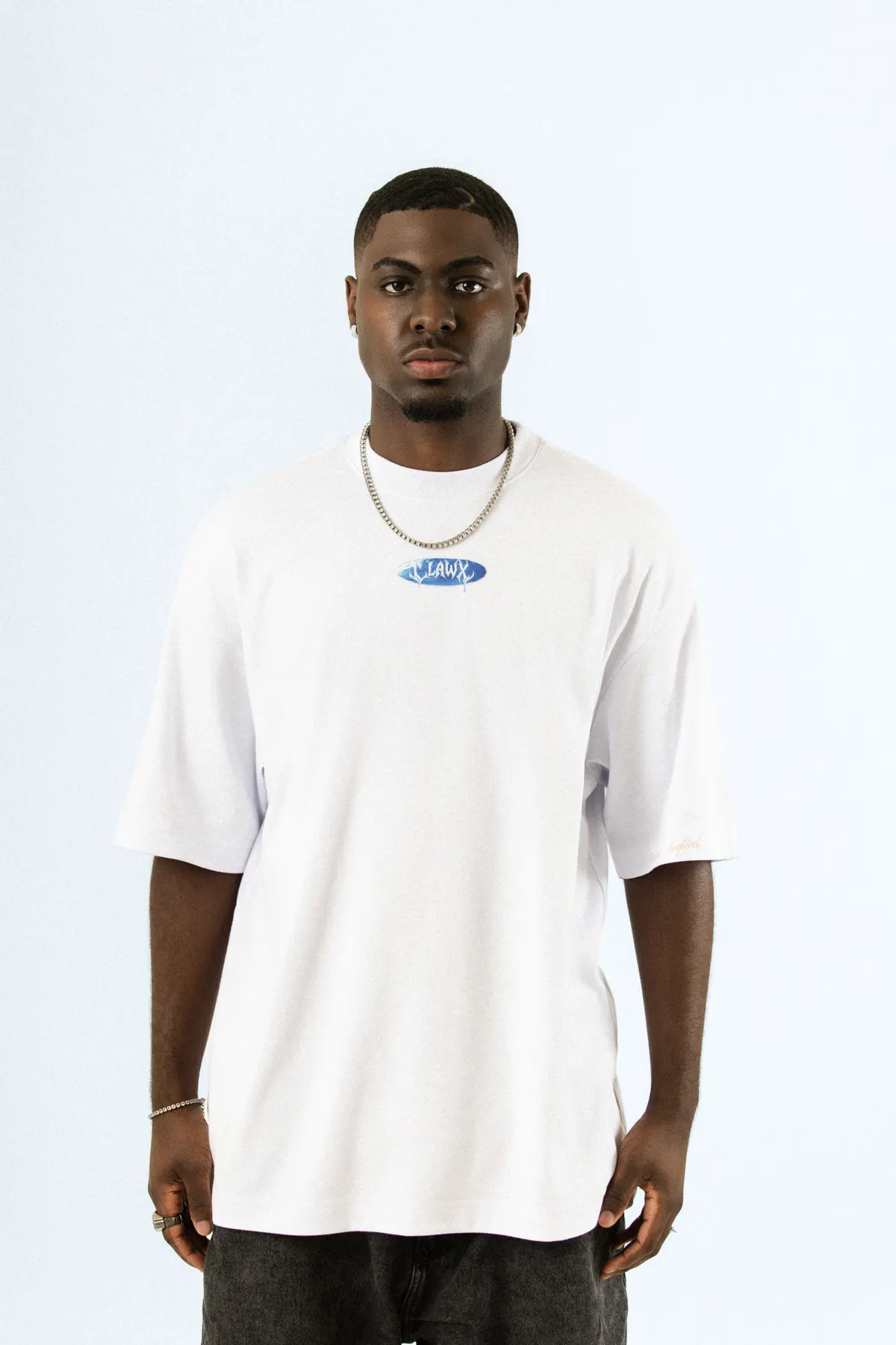 Modelo de corrente prateada, de frente, com a camiseta branca e a etiqueta azul oval no peito.